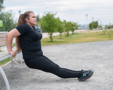Dışarıdaki banktan şınav çeken genç şişman kadın. Tombul kız spor yapıyor..