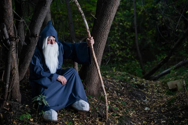Волшебник с длинной седой бородой и плащом в глубоком лесу. Пожилой человек в костюме ведьмы — стоковое фото
