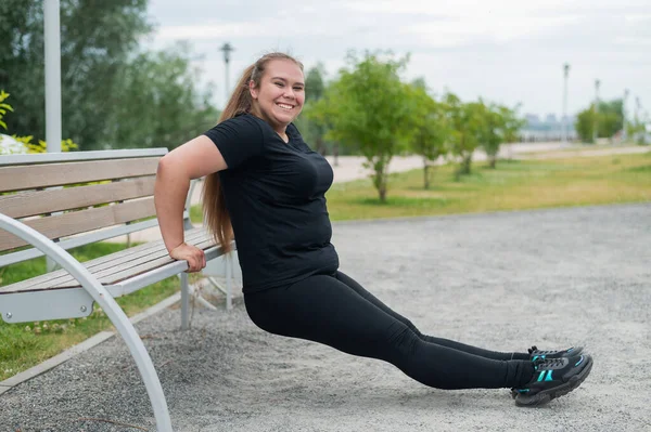 Junge dicke Frau macht Liegestütze von der Bank im Freien. Molliges Mädchen macht Fitnessübungen. — Stockfoto