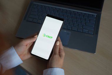 18 Ekim 2020 Rusya, Novosibirsk: Ekranda yeni Sberbank logosu olan bir kadın akıllı telefon tutuyor