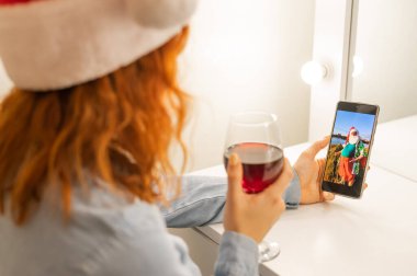 Kadın Noel Baba 'ya bir video görüşmesi yapıyor ve Noel zamanı kırmızı şarap içiyor.