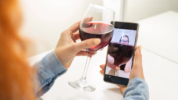 The women talk over video communication on the phone and drink red wine. The quarantined girl is not making a video call