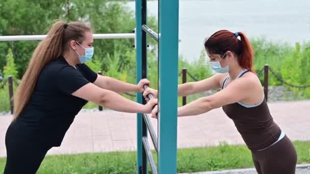 Две кавказки в защитных масках делают упражнения на открытой спортивной площадке. — стоковое видео
