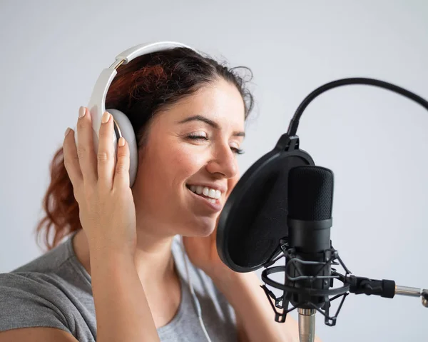 Egy nő fejhallgatóval felvesz egy dalt egy stúdióban. Az érzelmes lány örömmel énekel. — Stock Fotó