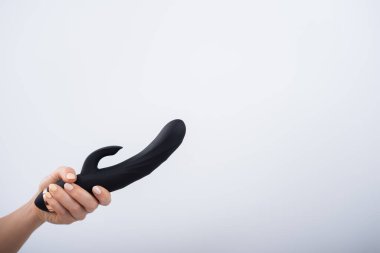 Faceless woman holding black dildo with clitoris stimulator on white background