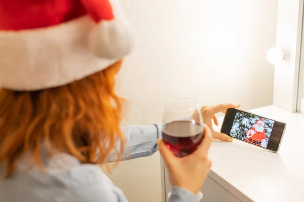 Жінка робить відеодзвінок Санті Клаусу і п'є червоне вино в різдвяний час — стокове фото