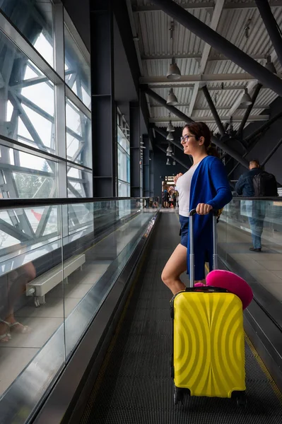 Kaukasierin auf einer waagerechten Rolltreppe mit einem Koffer am Flughafen. Ein Mädchen mit rosa Gepäck fährt auf einem fahrenden Bürgersteig — Stockfoto