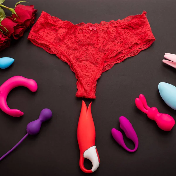 Vue du dessus de culotte de dentelle de femmes roses rouges et différents jouets sexuels. Collection de vibromasseurs multicolores sur fond noir. — Photo