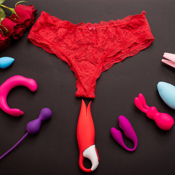 Top view of womens lace panties red roses and different sex toys. Collection of multicolored vibrators on a black background.