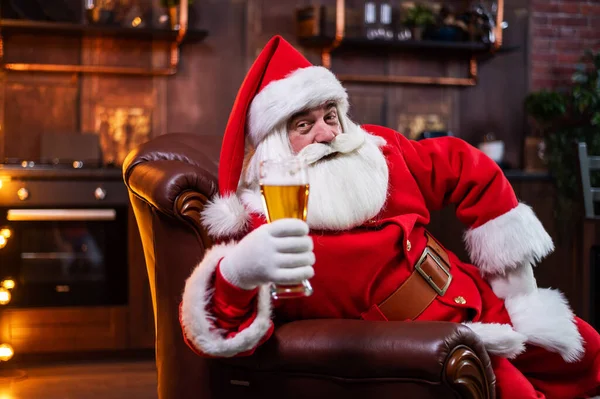 Święty Mikołaj pije piwo siedząc w skórzanym fotelu — Zdjęcie stockowe