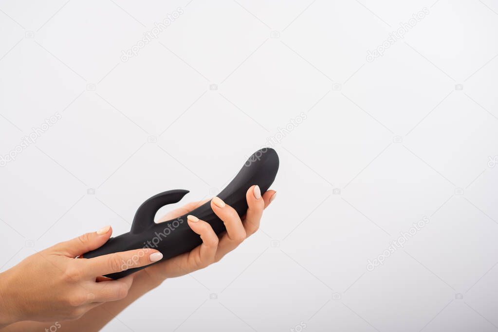 Faceless woman holding black dildo with clitoris stimulator on white background