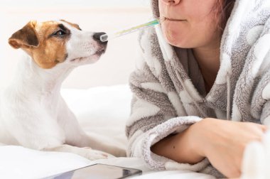 Beyaz kadın yatakta yatıyor ve vücut ısısını sözlü olarak ölçüyor. Ağzında cıva termometresi tutan bir kız.