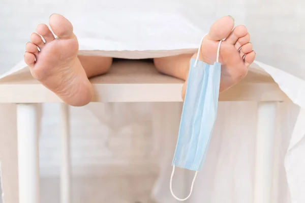 Close-up of dead men feet in a morgue with a medical mask on a toe. An unrecognizable woman has died from the coronavirus — Stock Photo, Image