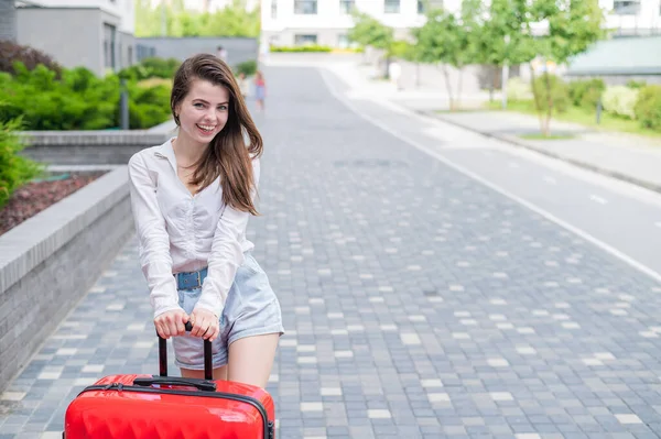 Eine schöne kaukasische Frau läuft mit einem großen Gepäck auf Rädern die Straße hinunter. Das Mädchen macht Urlaub — Stockfoto