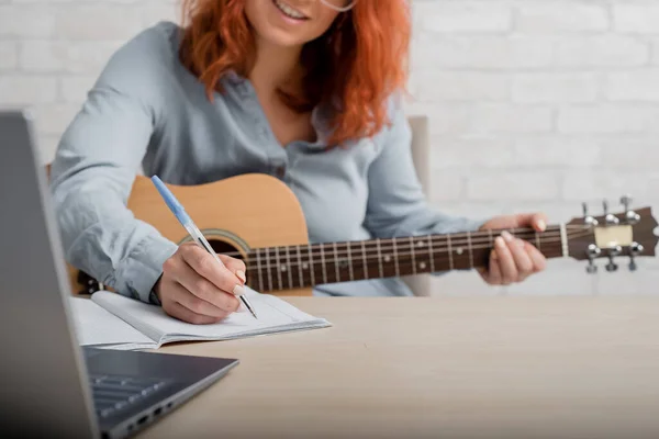 Eine Frau mit Gitarre schreibt Notizen in ein Notizbuch. Das Mädchen komponiert ein Lied — Stockfoto