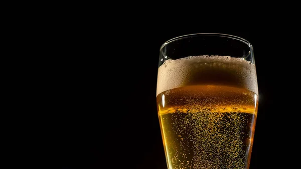 Detailní záběr čerstvě pěnícího světlého piva ve sklenici na tmavém pozadí — Stock fotografie