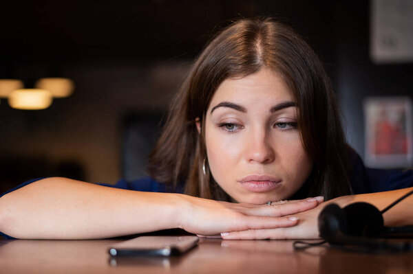 Грустная женщина положила голову на стол и ждет телефонного звонка.