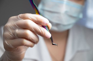 Maskeli Lashmaker cımbızla bir sürü kirpik tutuyor. Güzellik salonunda çalışan bir ustanın yakın çekimi.