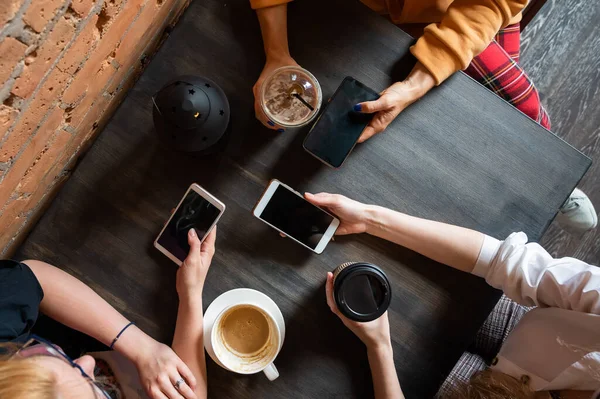 Visão superior de mãos femininas com smartphones e xícaras de café em uma mesa em um café. Três namoradas bebendo café. — Fotografia de Stock