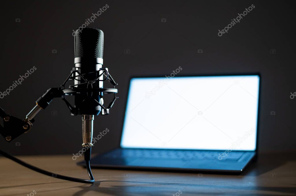 Professional microphone and laptop with white screen in the dark. Equipment in a recording and broadcasting studio