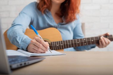 Gitarlı bir kadın deftere notlar yazar. Kız bir şarkı yazıyor.