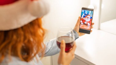 Kadın Noel Baba 'ya bir video görüşmesi yapıyor ve Noel zamanı kırmızı şarap içiyor.