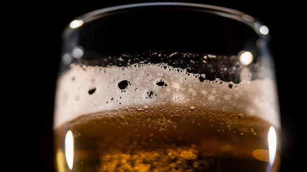Detailní záběr čerstvě pěnícího světlého piva ve sklenici na tmavém pozadí — Stock fotografie