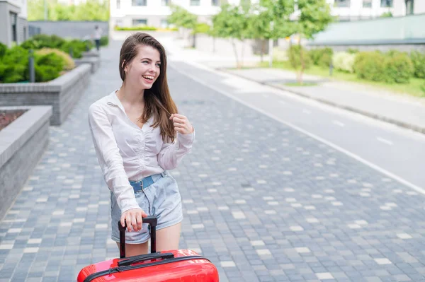Eine schöne kaukasische Frau läuft mit einem großen Gepäck auf Rädern die Straße hinunter. Das Mädchen macht Urlaub — Stockfoto