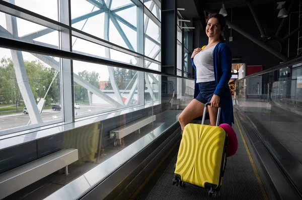 Kaukasierin auf einer waagerechten Rolltreppe mit einem Koffer am Flughafen. Ein Mädchen mit rosa Gepäck fährt auf einem fahrenden Bürgersteig — Stockfoto