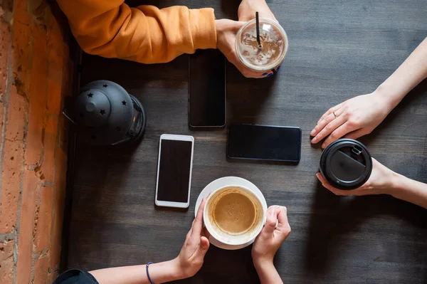 Visão superior de mãos femininas com smartphones e xícaras de café em uma mesa em um café. Três namoradas bebendo café. — Fotografia de Stock