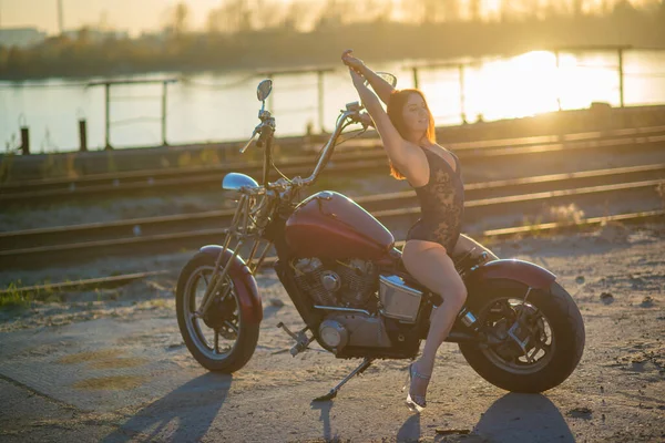 Femme aux cheveux rouges en lingerie sexy en talons hauts s'assoit sur une moto. Attrayant fille aux cheveux roux assis sur une moto au coucher du soleil — Photo