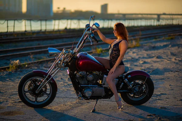 Mulher de cabelos vermelhos em lingerie sexy em salto alto senta-se em uma motocicleta. Atraente menina ruiva senta-se em uma motocicleta ao pôr do sol — Fotografia de Stock