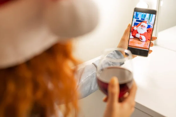Жінка робить відеодзвінок Санті Клаусу і п'є червоне вино в різдвяний час — стокове фото