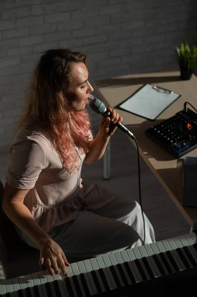 Expressive female singer has a video blog on a laptop. Portrait of a girl recording a song on a web camera and composing on a synthesizer. Online music lessons. Distance learning in quarantine.