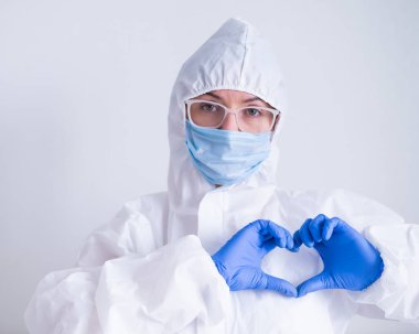Koruyucu kıyafetli kadın doktor kalbi bir jestle gösteriyor. Hasta sağlığı konsepti