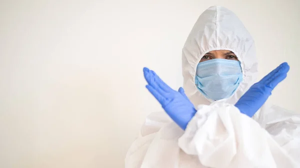 Ženská doktorka v ochranném obleku ukazuje zástavu se zkříženýma rukama. Zastavte koronavirus. — Stock fotografie