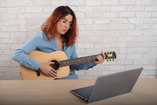 Blanke vrouw die online gitaar leert spelen. Het meisje zit in quarantaine op afstand muziek te bestuderen. — Stockfoto