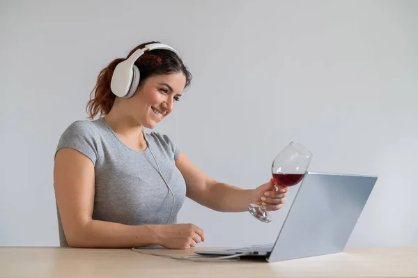 Femme caucasienne dans un casque griller avec un verre de vin rouge lors d'un appel vidéo à la maison. Télécommunication isolée — Photo
