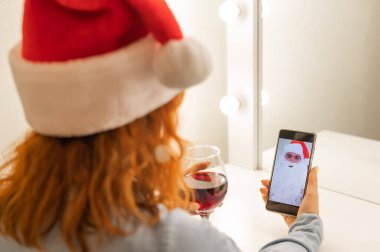 Kadın Noel Baba 'ya bir video görüşmesi yapıyor ve Noel zamanı kırmızı şarap içiyor.