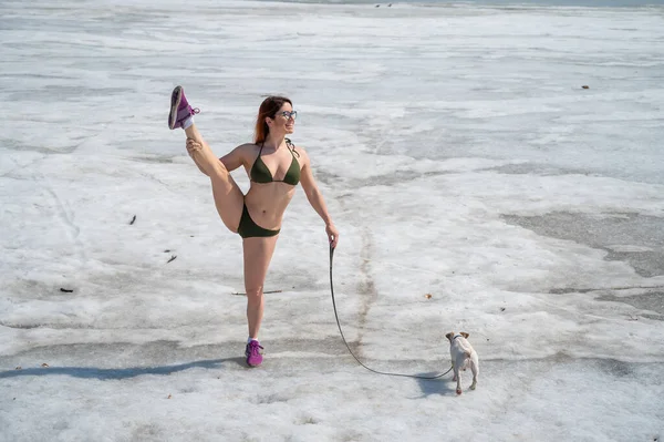 Bikinili bir kadın karda bir köpekle yürür. — Stok fotoğraf