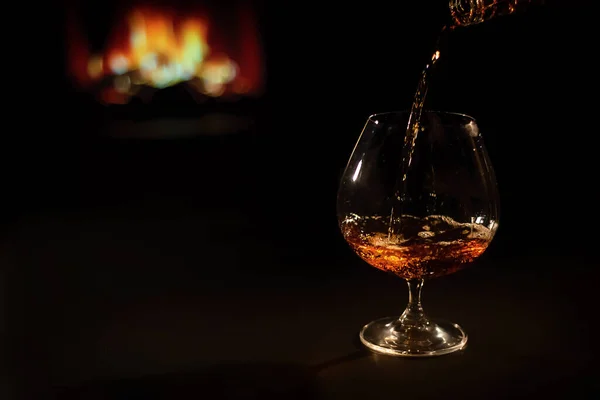 Vor dem Hintergrund des Kamins Brandy in ein Glas gießen — Stockfoto