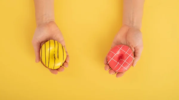 Mãos femininas com donuts em um fundo amarelo. Espaço de cópia. — Fotografia de Stock