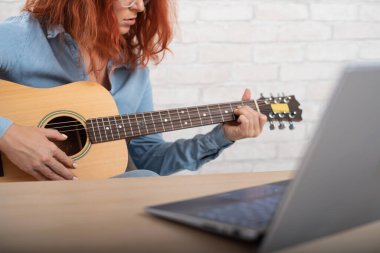 Genç bir kadın dizüstü bilgisayardan gitar çalmayı öğreniyor. Çevrim içi müzik dersleri