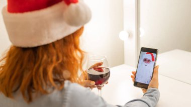 Kadın Noel Baba 'ya bir video görüşmesi yapıyor ve Noel zamanı kırmızı şarap içiyor.