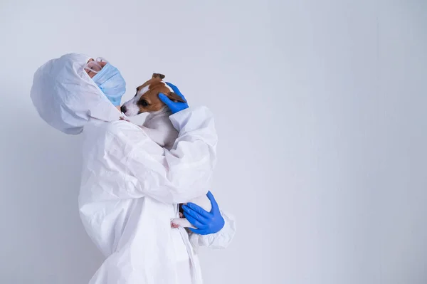 Žena v ochranném obleku a masce drží psa Jack Russell teriér na bílém pozadí — Stock fotografie