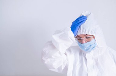 Koruyucu kıyafetli ve tıbbi maskeli bir kadın kafasını tutuyor. İşte sorunları olan bir doktor virüs uzmanı.