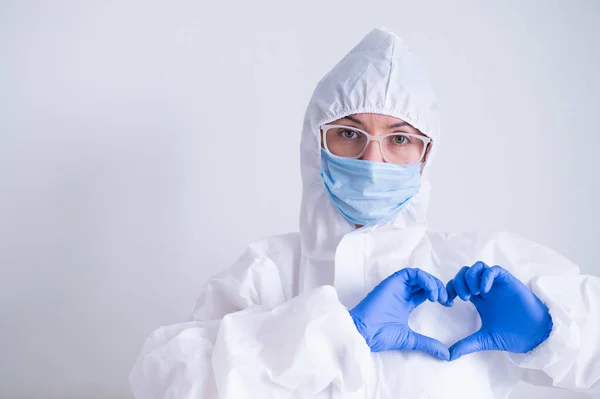 Female doctor in a protective suit shows the heart with a gesture. Patient health care concept — Stock Photo, Image