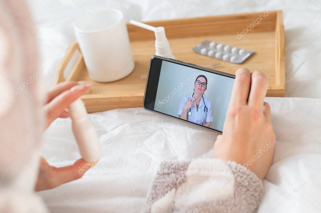 A woman lies at home in bed and consults on a smartphone. Medicine online