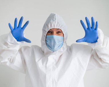 Koruyucu giysili bir kadın ve korkunç bir buruşukluğu olan tıbbi bir maske. Doktor avuçlarını yüzüne dayadı ve korktu.