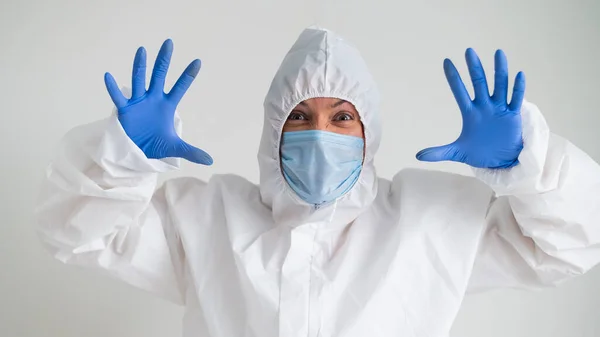 Eine Frau in Schutzanzug und medizinischer Maske mit schrecklicher Fratze. Der Sanitäter hält sich die Handflächen vor das Gesicht und bekommt Angst — Stockfoto